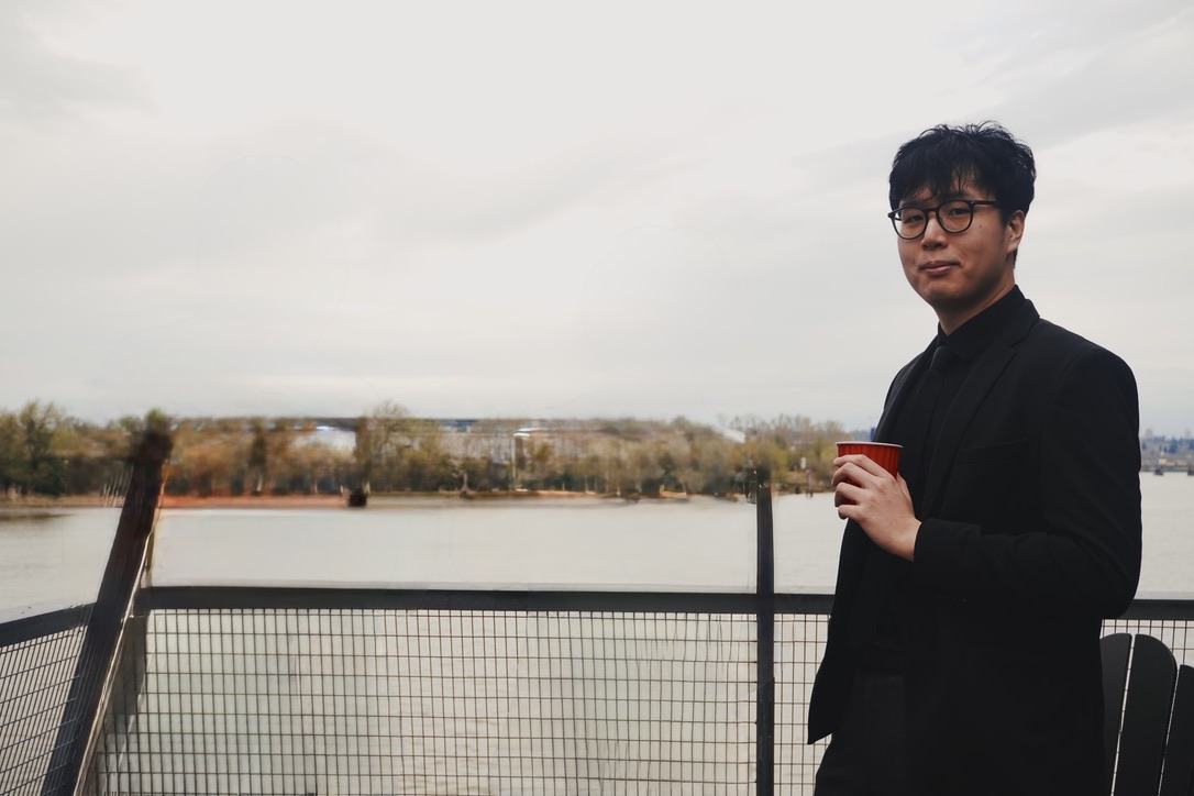 Portrait of Kenten Au holding a cup on a riverside terrace